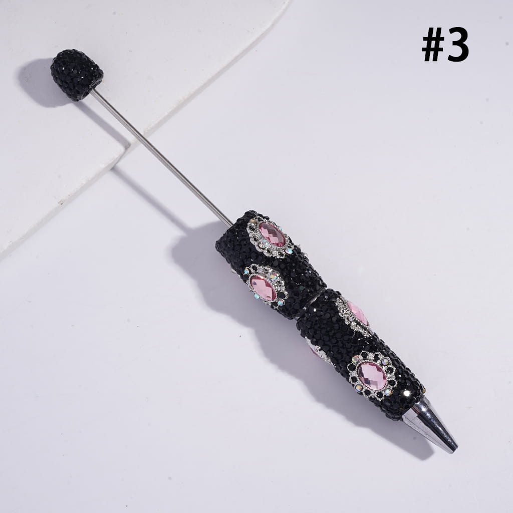 Decorative pen with black textured grip and pink gemstones on a white background