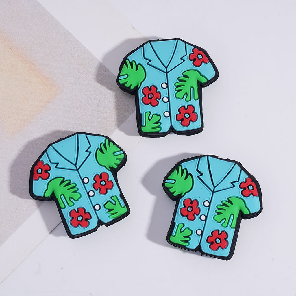 Three colorful shirt-shaped pins with floral and leaf designs on a light background