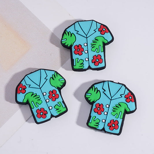 Three colorful shirt-shaped pins with floral and leaf designs on a light background