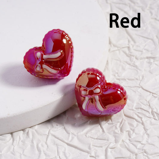 Heart-shaped earrings with a bow design on a textured white surface, labeled 'Red'.

