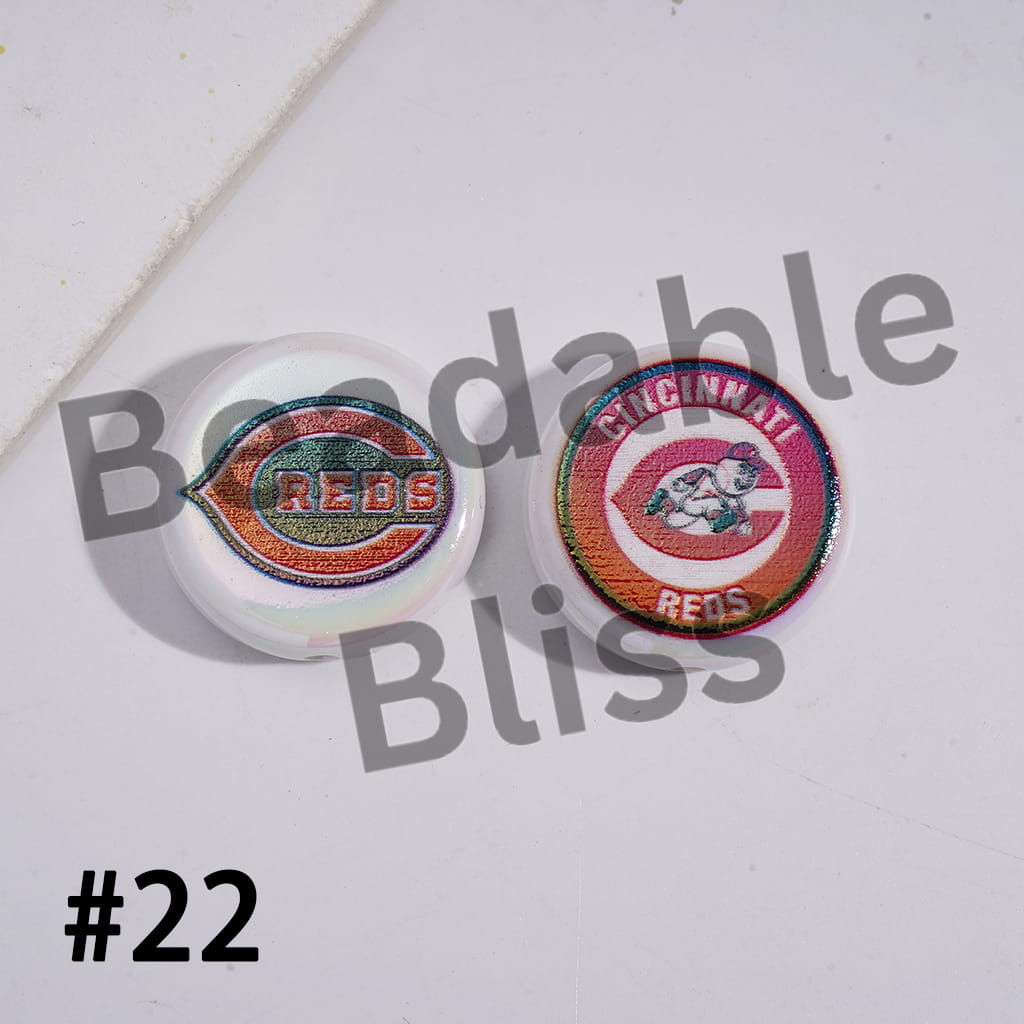 Two Cincinnati Reds earrings on a white surface with 'Bodable Bliss' branding.

