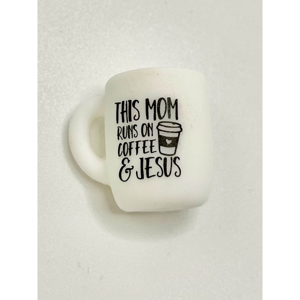A white ceramic coffee mug with black text and a graphic that reads 'This Mom Runs on Coffee & Jesus'.

