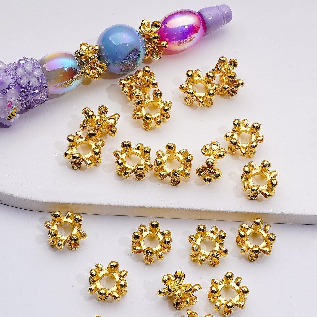 Gold bead caps on a white surface with colorful beads in the background

