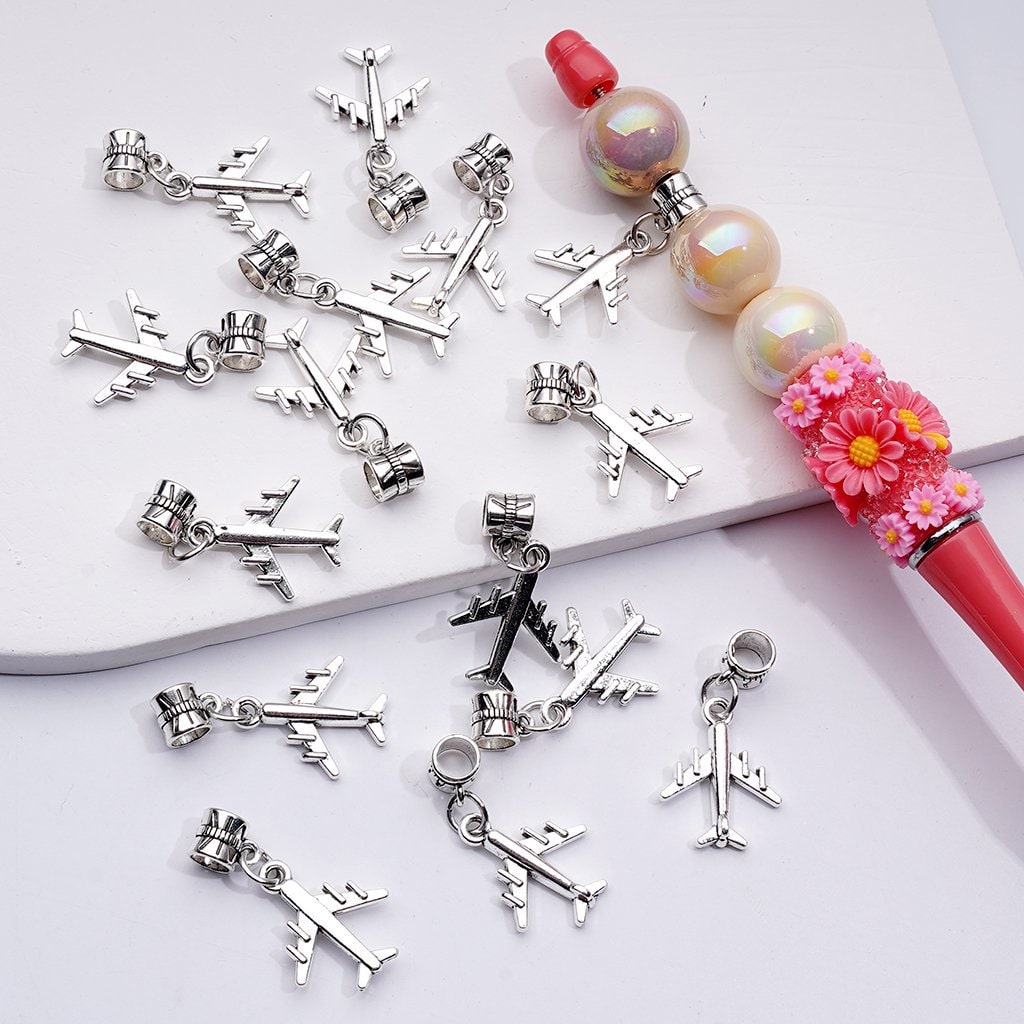 Silver airplane charms on a white surface with a decorative pen.

