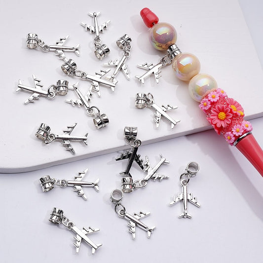 Silver airplane charms on a white surface with a decorative pen.

