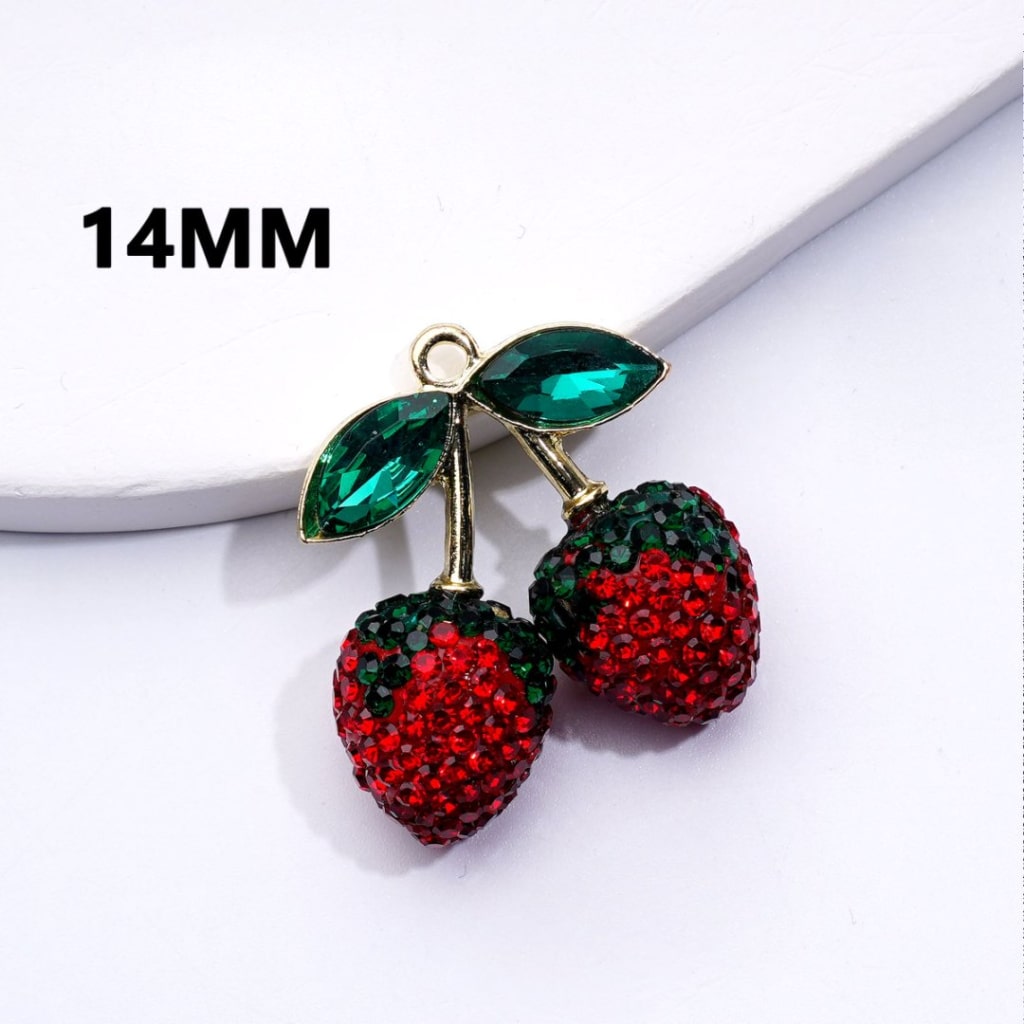 Two gold alloy clay pendants shaped like strawberries with red fruit and green leaves on a white surface.

