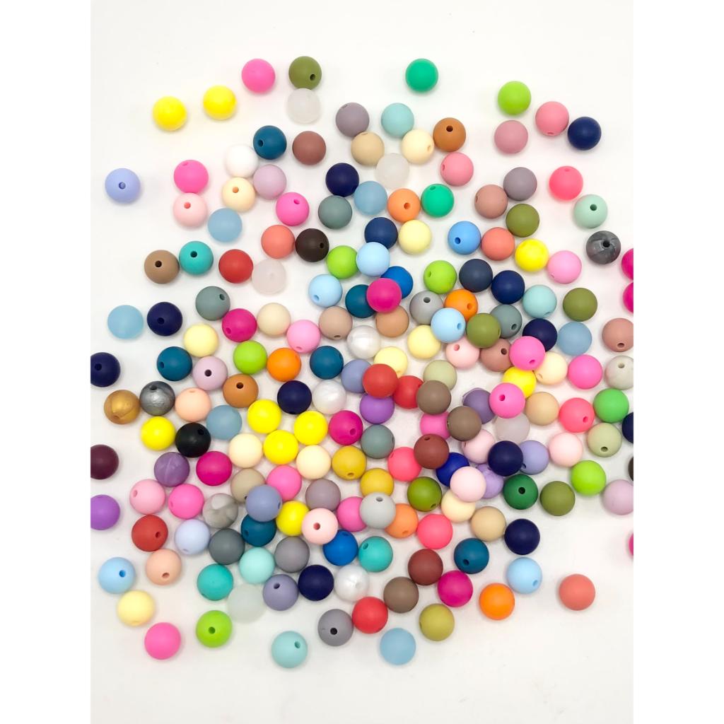 A collection of small silicone beads in various solid colors, scattered on a surface.

