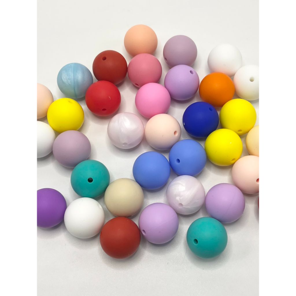 A collection of round silicone beads in various solid colors including red, blue, green, yellow, purple, pink, gray, and white.

