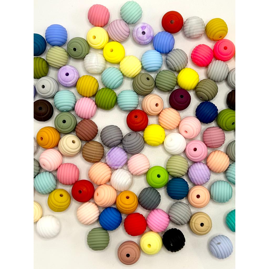 A collection of multicolored silicone beads arranged on a surface, varying in colors and patterns, intended for use in crafting and jewelry making.

