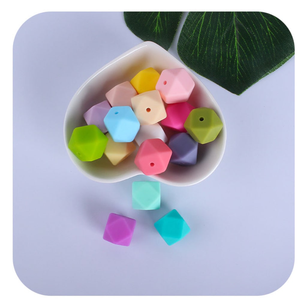 A collection of solid colored hexagon silicone beads in various colors displayed in a heart-shaped bowl.


