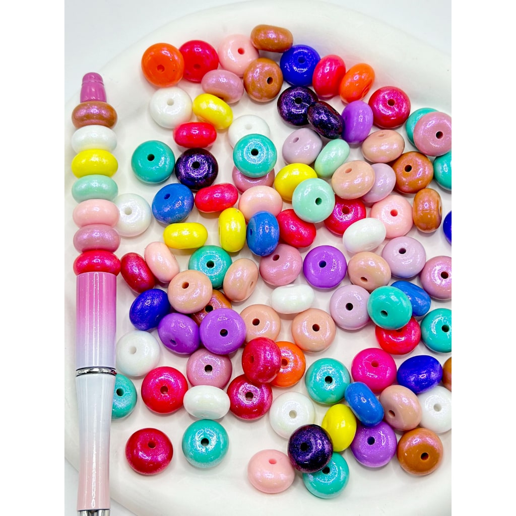 A collection of multicolored round silicone beads with a hole in the center, displayed on a surface with a pen for scale.

