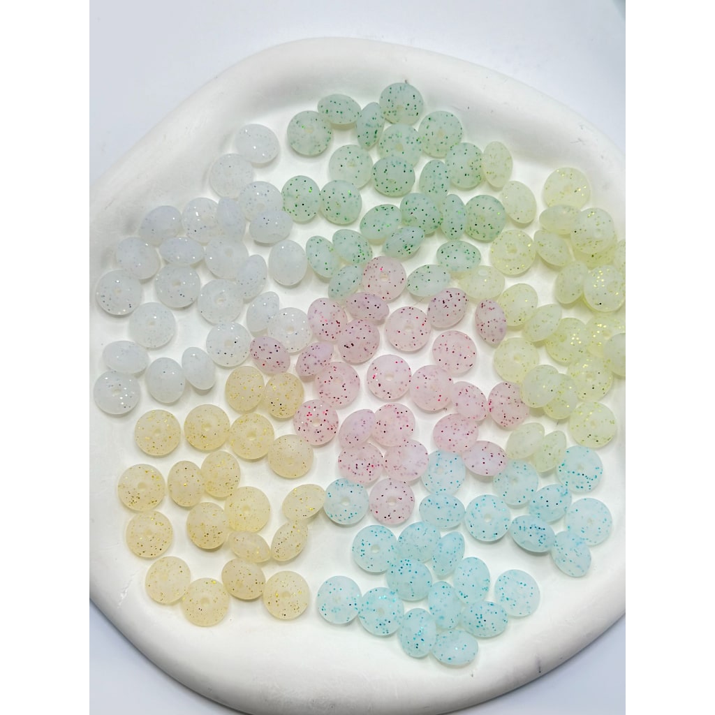 A collection of round silicone beads in various colors including white, pink, blue, and green, displayed on a flat surface.

