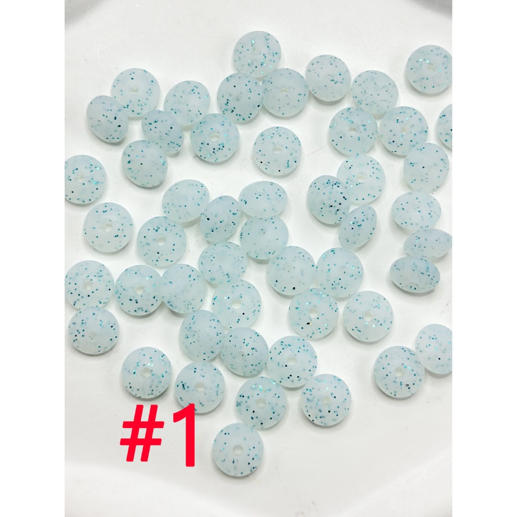 A collection of round silicone beads in various colors including white, pink, blue, and green, displayed on a flat surface.

