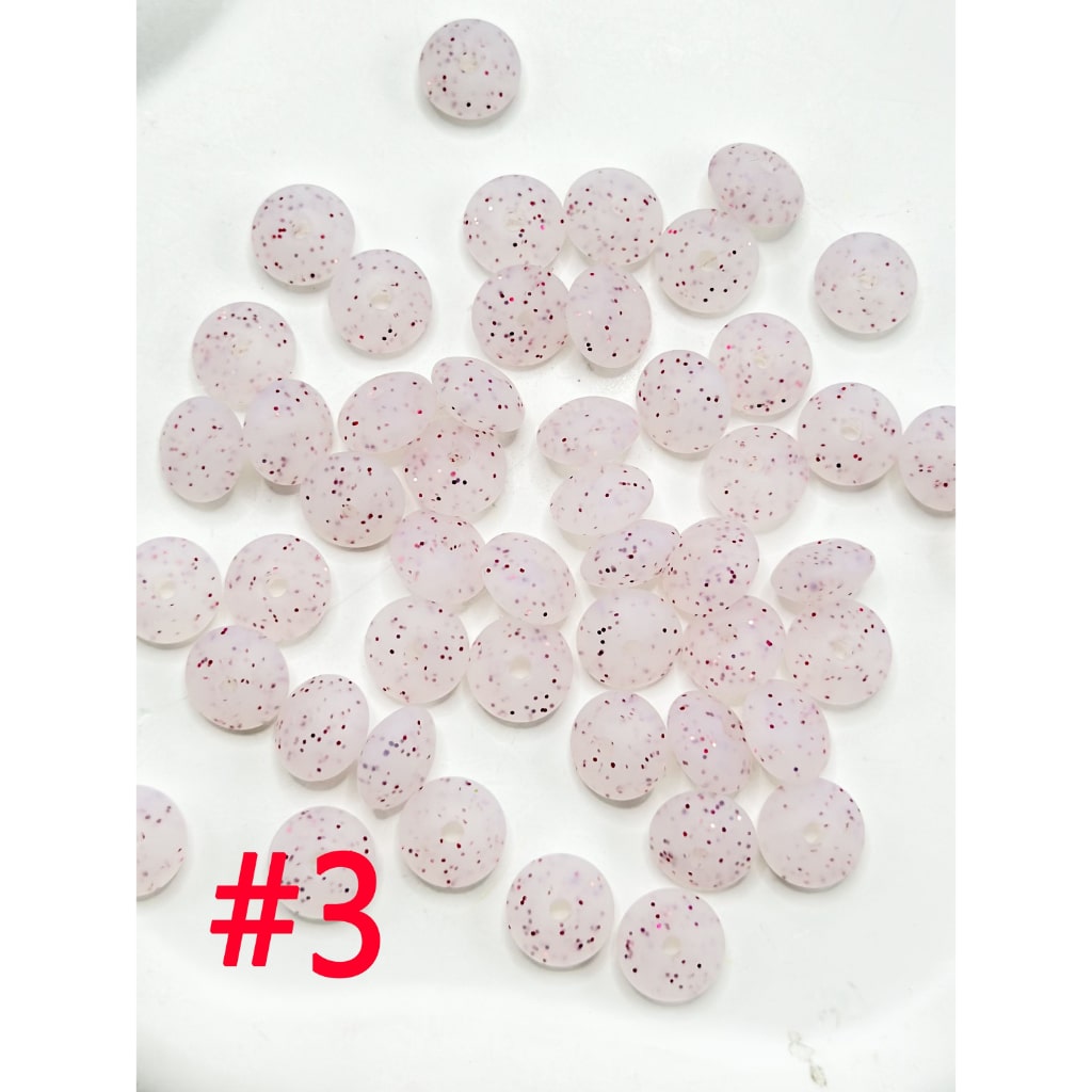 A collection of round silicone beads in various colors including white, pink, blue, and green, displayed on a flat surface.

