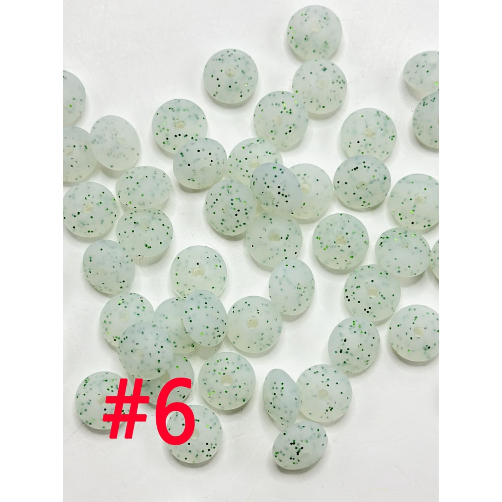 A collection of round silicone beads in various colors including white, pink, blue, and green, displayed on a flat surface.

