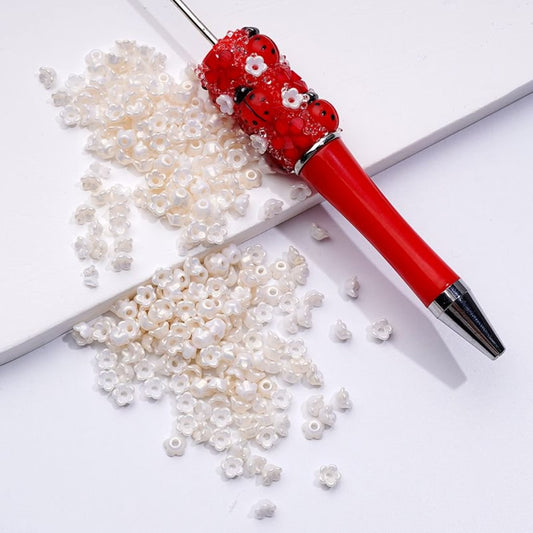 A red pen with a decorative pearl and flower design on the top, surrounded by white bead-like embellishments on a white surface.

