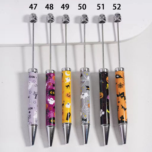 A set of plastic beadable pens with Halloween-themed decorations, including pumpkins, ghosts, and bats, displayed in various colors.


