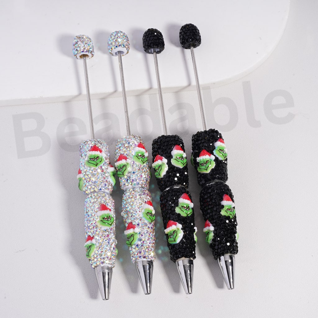 Set of decorative pens with Grinch designs and rhinestone accents on a white background.

