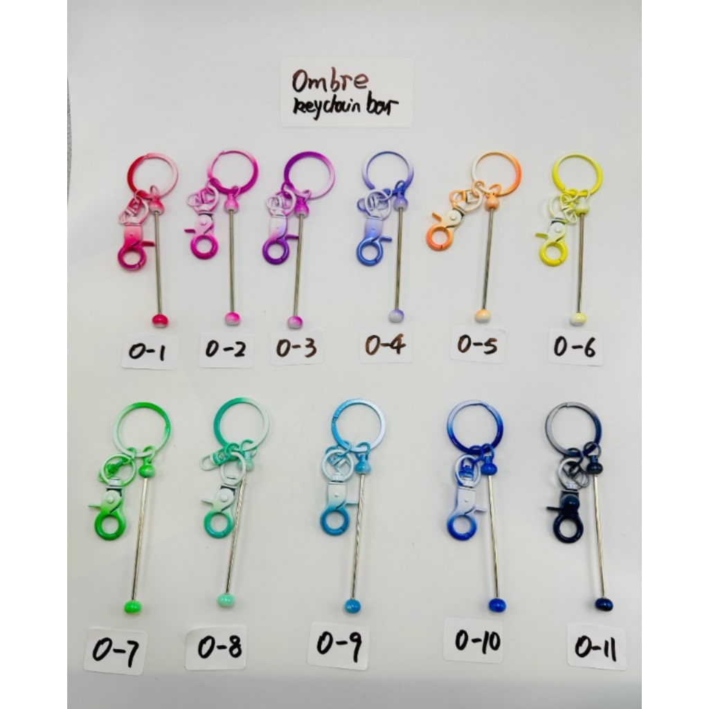 A collection of colorful metal beadable keychains with a bar and mini lobster clasp, laid out on a white surface, labeled with numbers 0-11.

