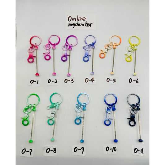 A collection of colorful metal beadable keychains with a bar and mini lobster clasp, laid out on a white surface, labeled with numbers 0-11.

