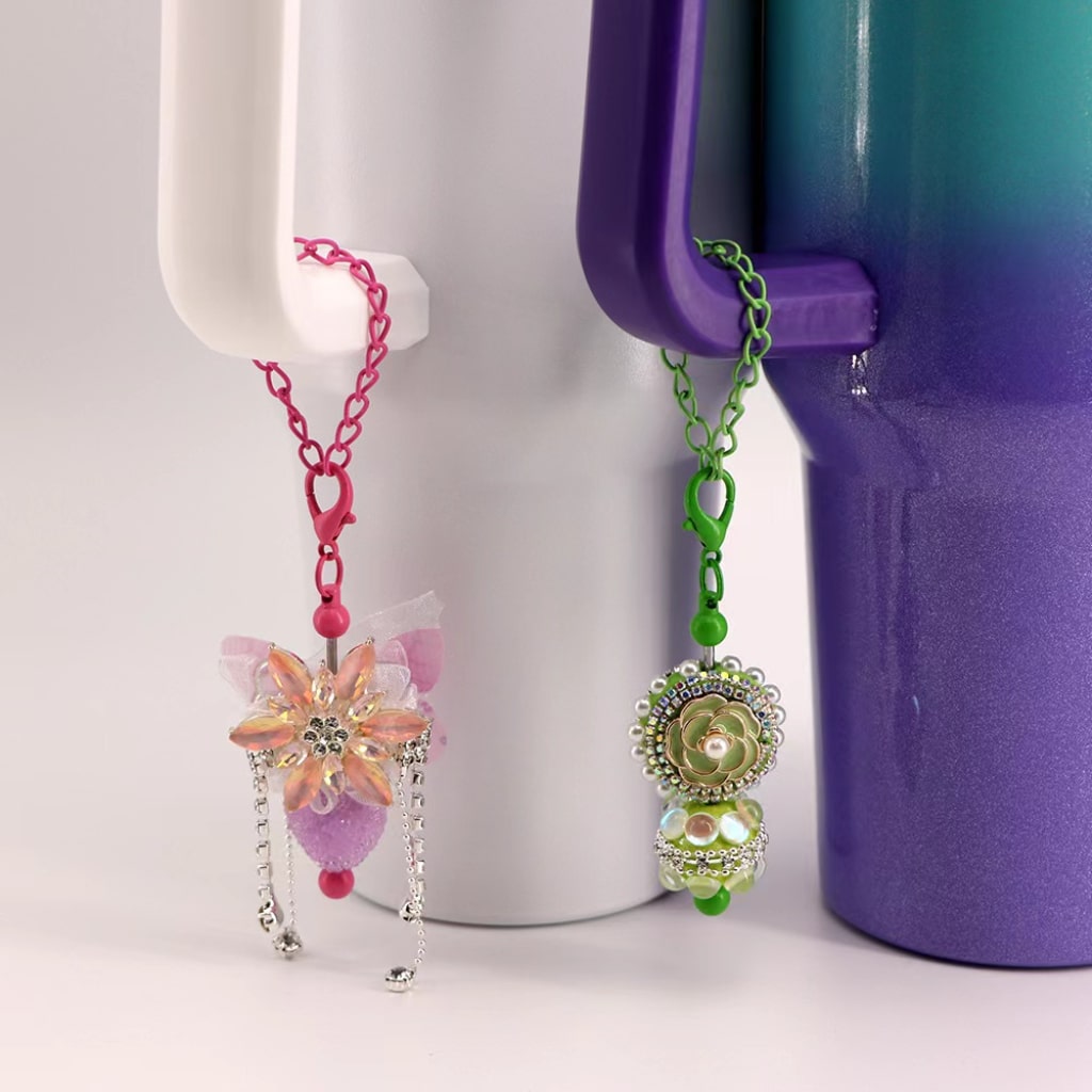 A lobster clasp in solid colors attached to a chain, designed to be used as a pendant holder for cups and tumblers, displayed against a white and purple background.

