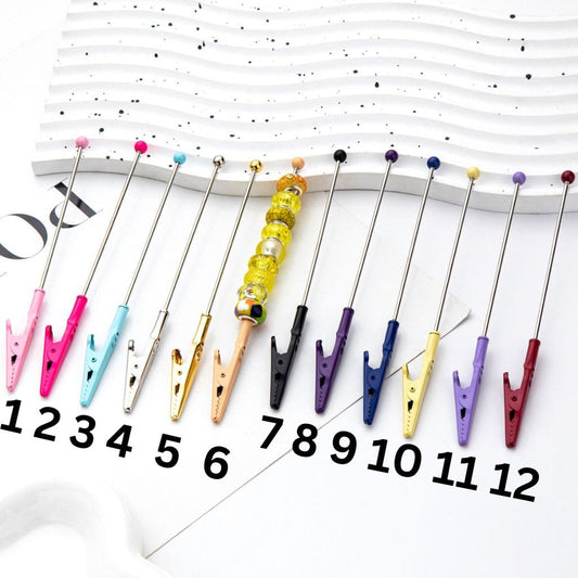 A selection of colorful alligator clips with beadable ends in various colors including pink, blue, yellow, green, purple, and silver.

