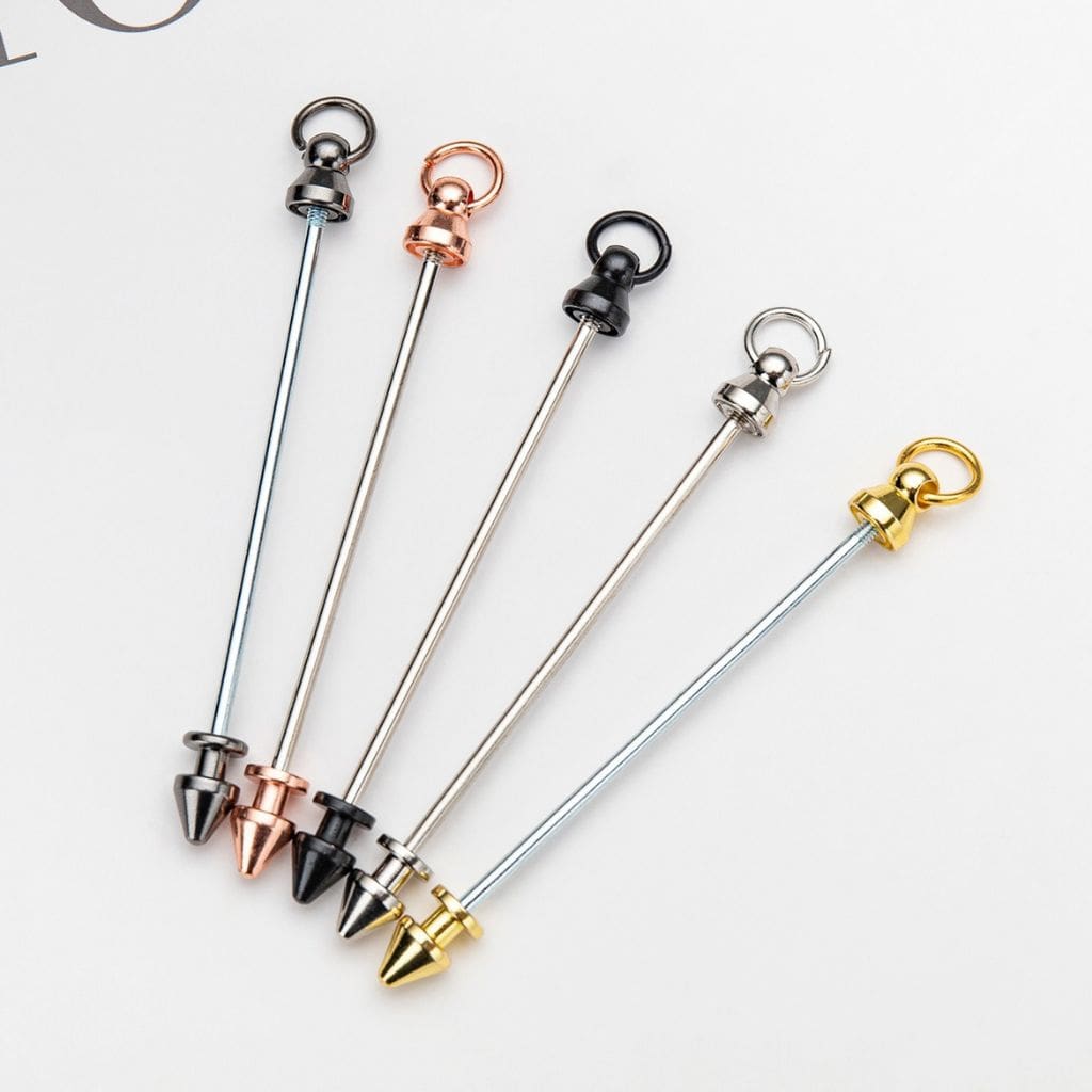 A selection of metal keychains with beadable bars in various colors including silver, rose gold, black, gold, and gunmetal.

