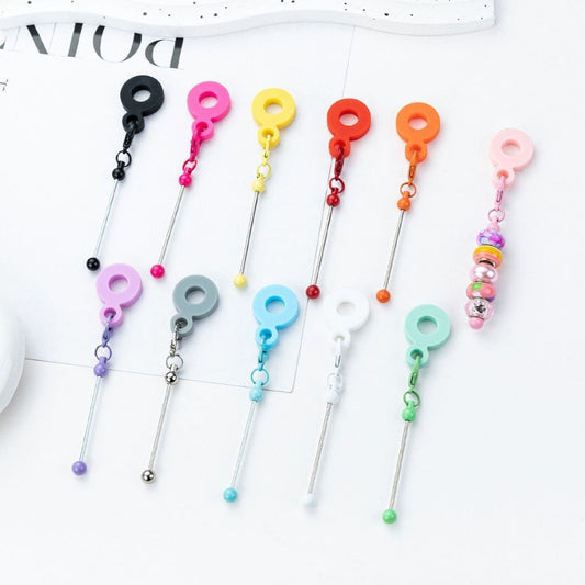 A collection of beadable metal bars in various solid colors, each with a carabiner hook and silicone ring attached.

