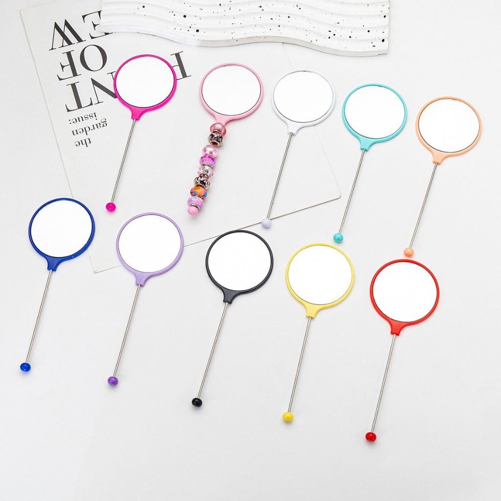 A collection of mini round makeup mirrors with keychain bars in various solid colors displayed on a table.

