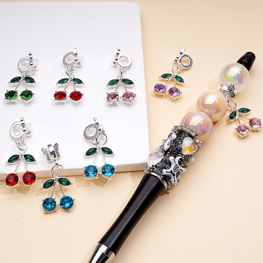 Decorative pen with gemstone-encrusted cherry pendants on a beige background

