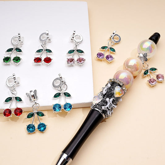 Decorative pen with gemstone-encrusted cherry pendants on a beige background

