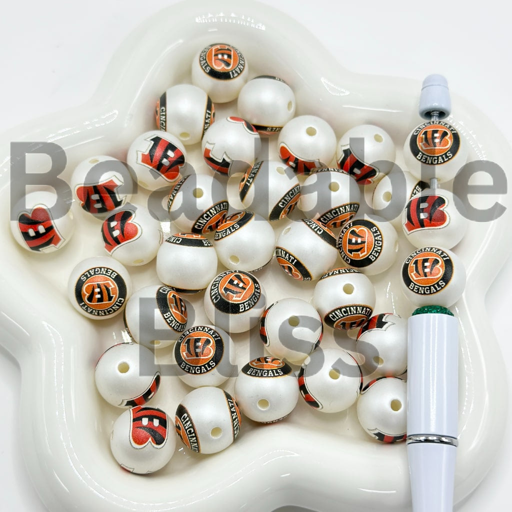 White beads with Cincinnati Bengals logo in a white dish with a pen

