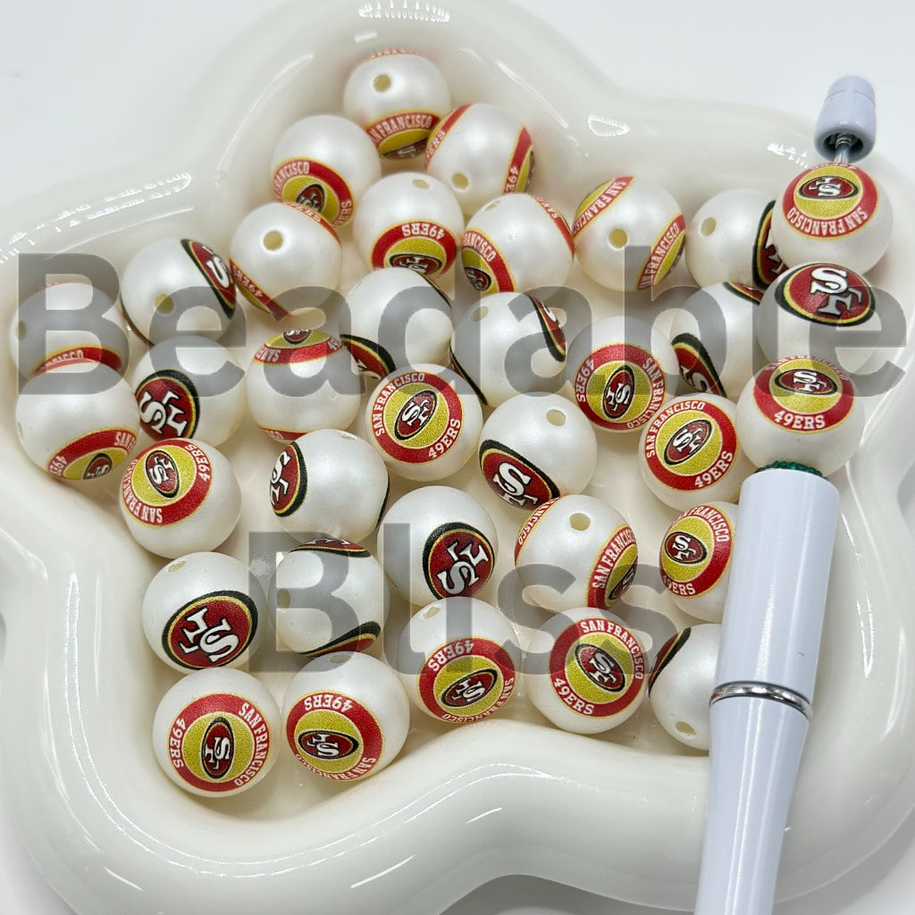 White beads with San Francisco 49ers logos on a white dish with a pen.

