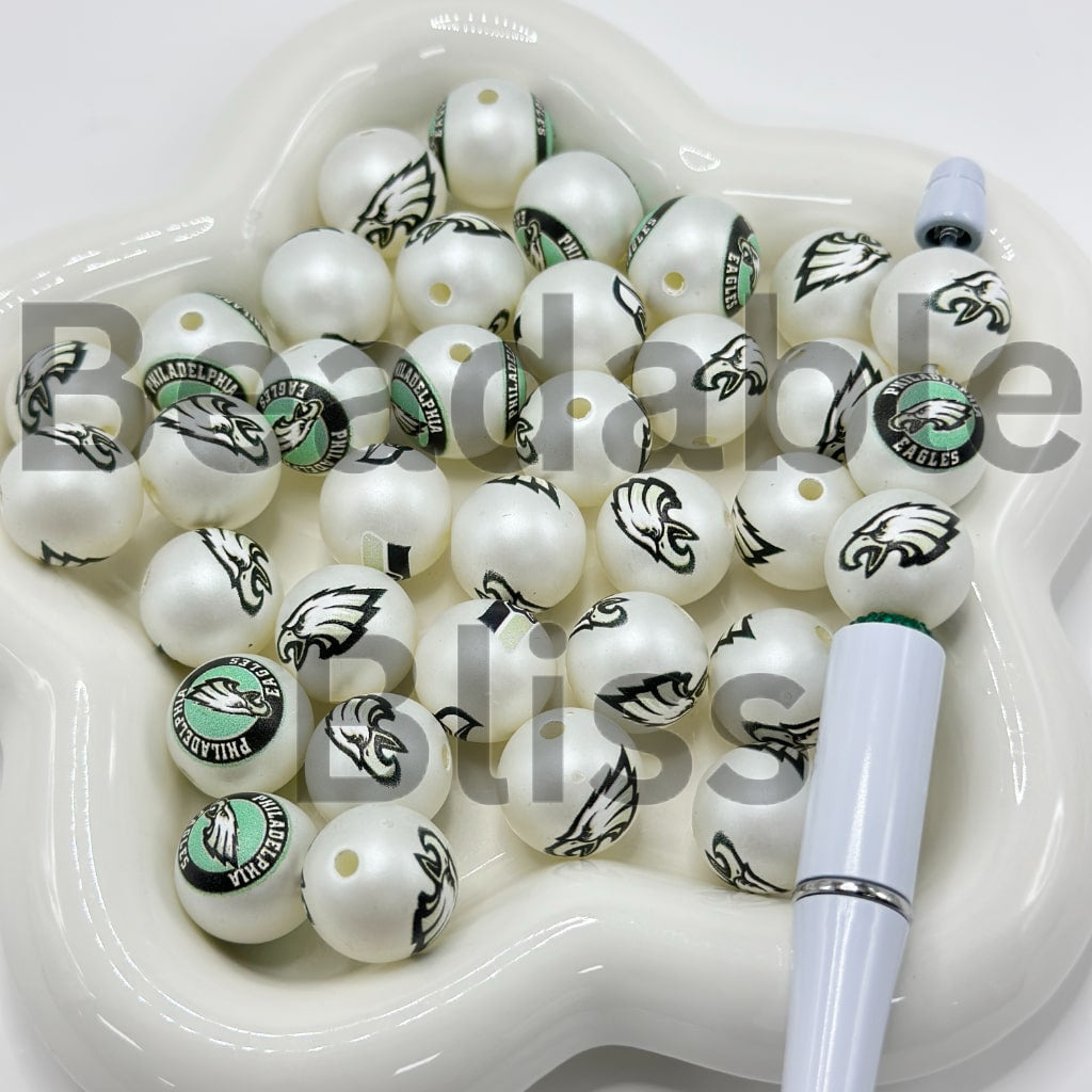 White beads with Philadelphia Eagles logos in a white dish with a pen

