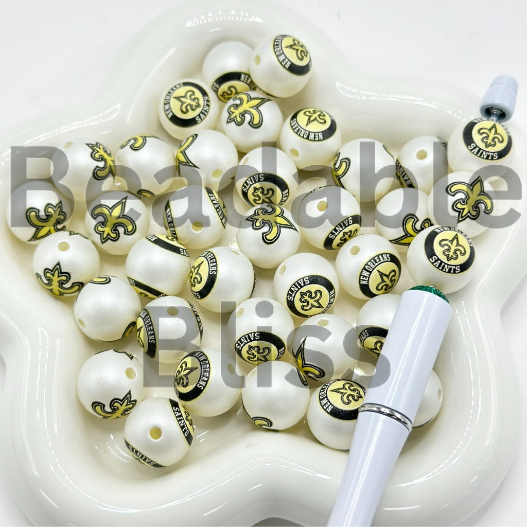 White beads with black and gold designs in a white container with a pen on a white background

