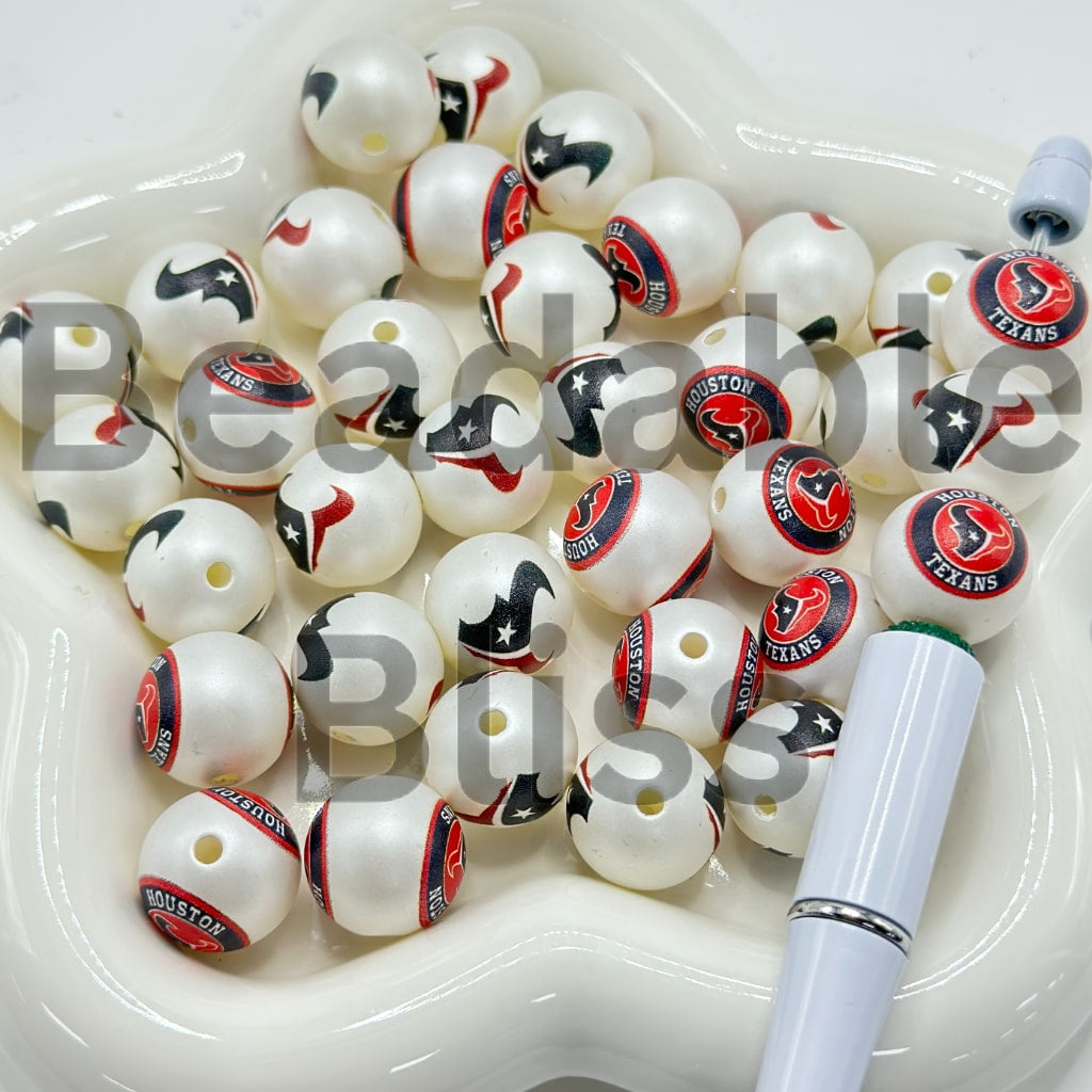 White beads with Houston Texans logos on a white plate with a pen.

