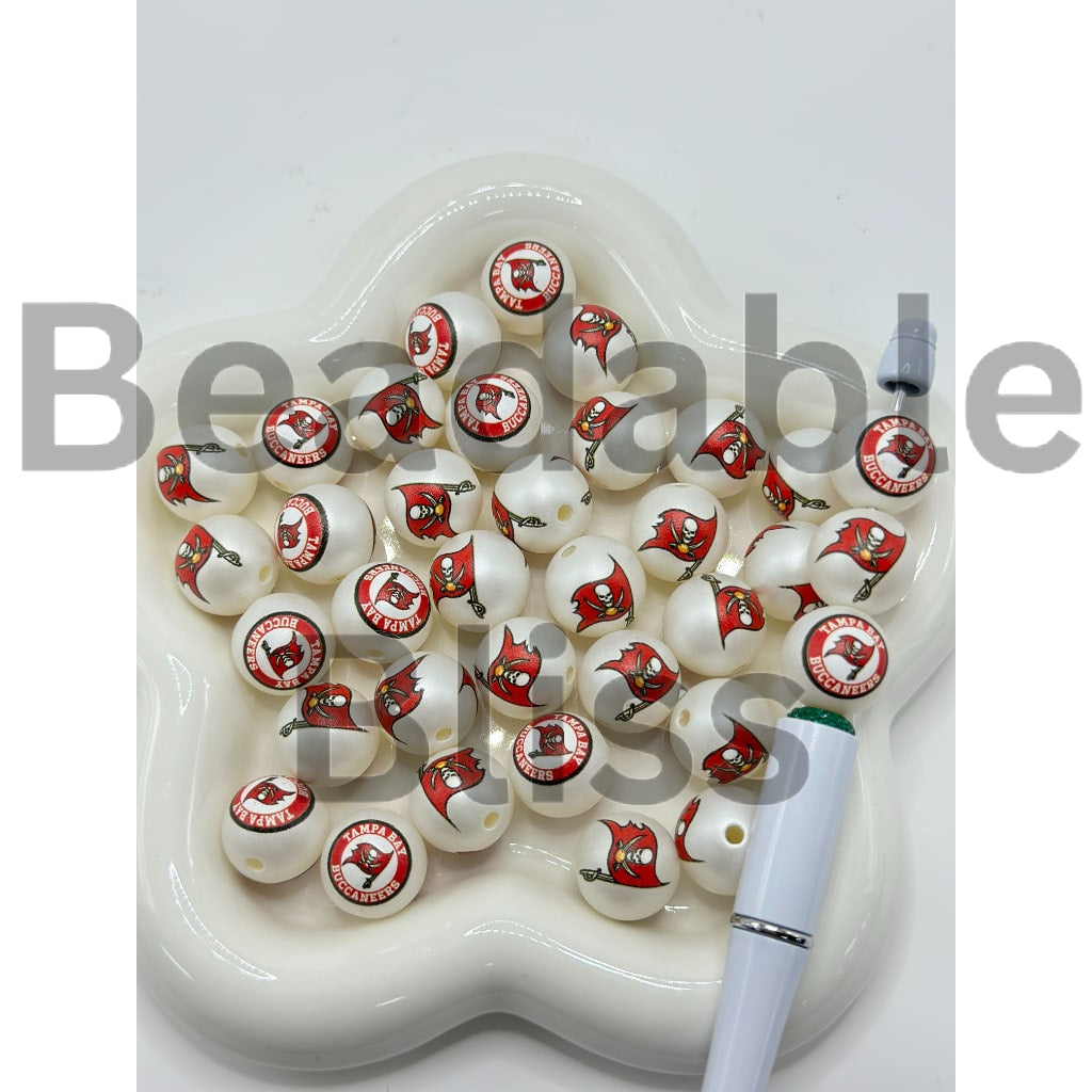 White beads with red and black logos on a white dish with a pen next to it.

