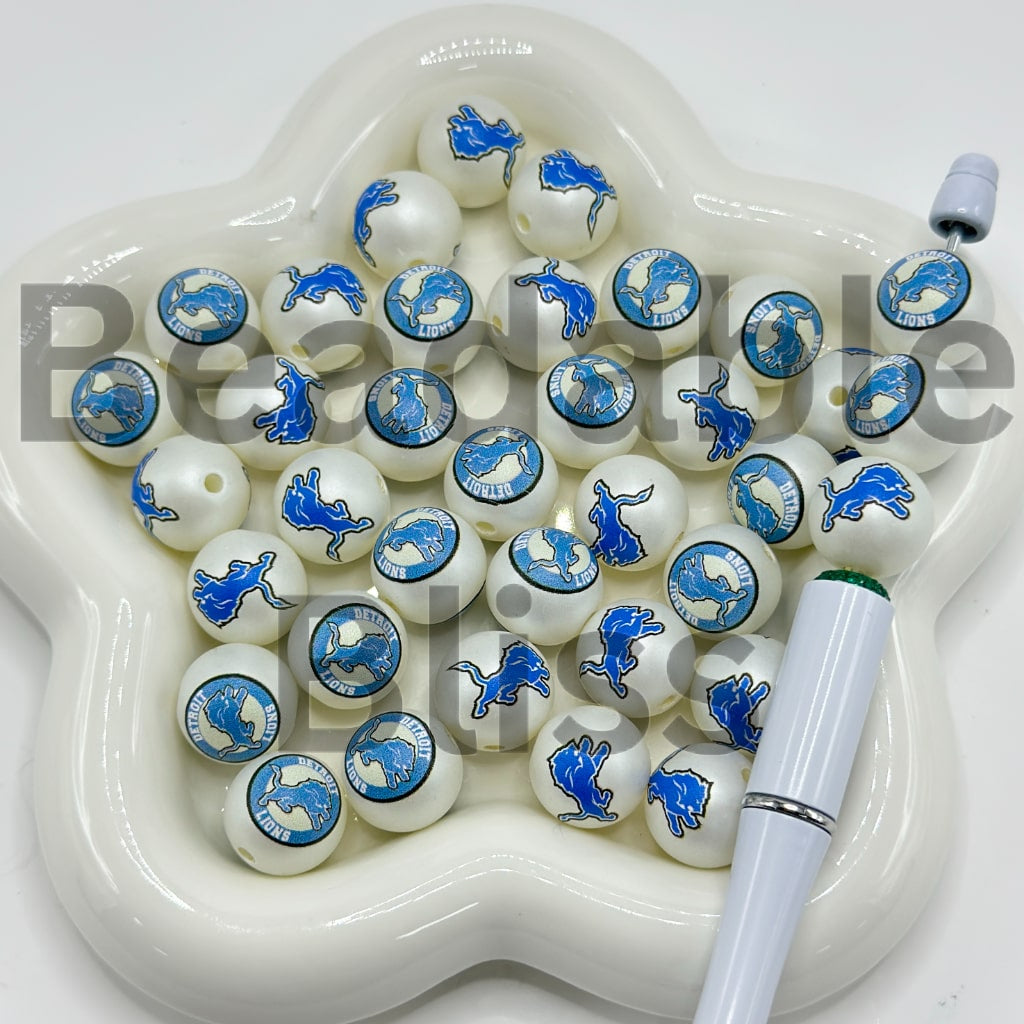 White beads with blue designs on a white dish with a white pen.

