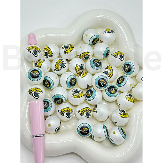 White beads with sports team logos on a white heart-shaped dish with a pink pen.

