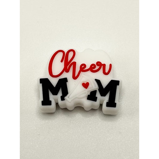 A silicone bead with the text 'Cheer MOM' written in red and white, with a heart symbol replacing the letter 'O'.

