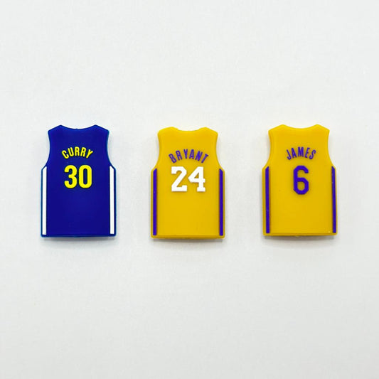 Three silicone beads designed to look like basketball jerseys in blue, yellow, and white colors with the numbers 30, 24, and 6 printed on them.

