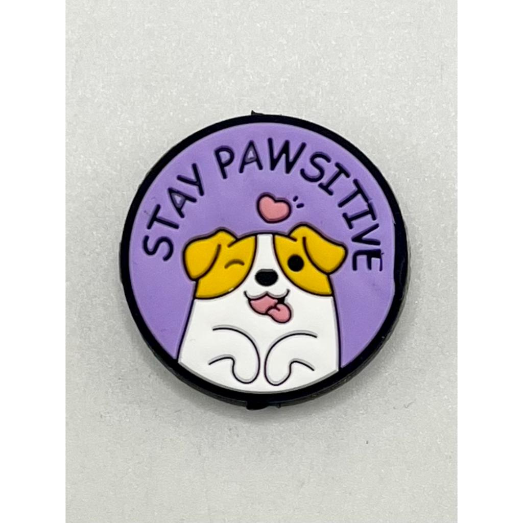 A silicone focal bead featuring a cartoon dog with the phrase 'STAY PAWSITIVE' written around it.

