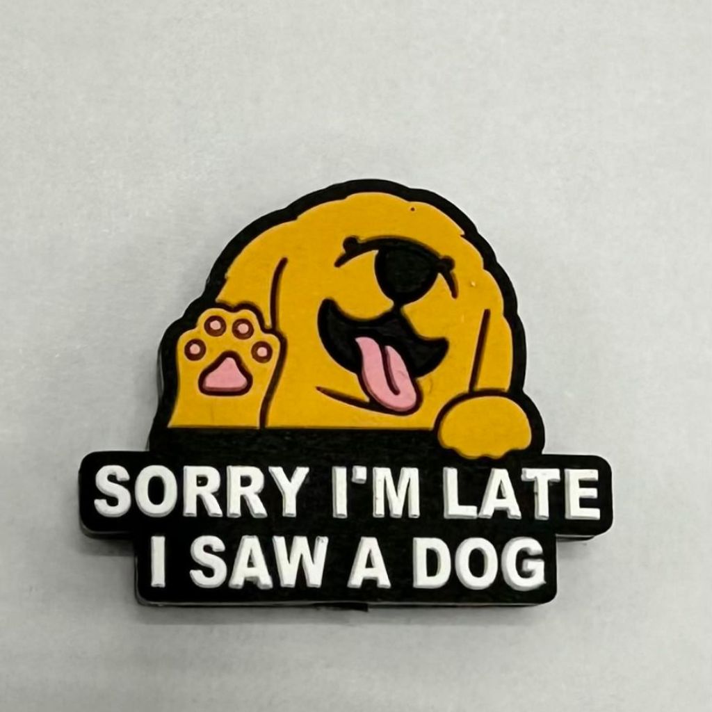 A yellow silicone bead in the shape of a puppy with the text 'SORRY I'M LATE I SAW A DOG' printed on it.

