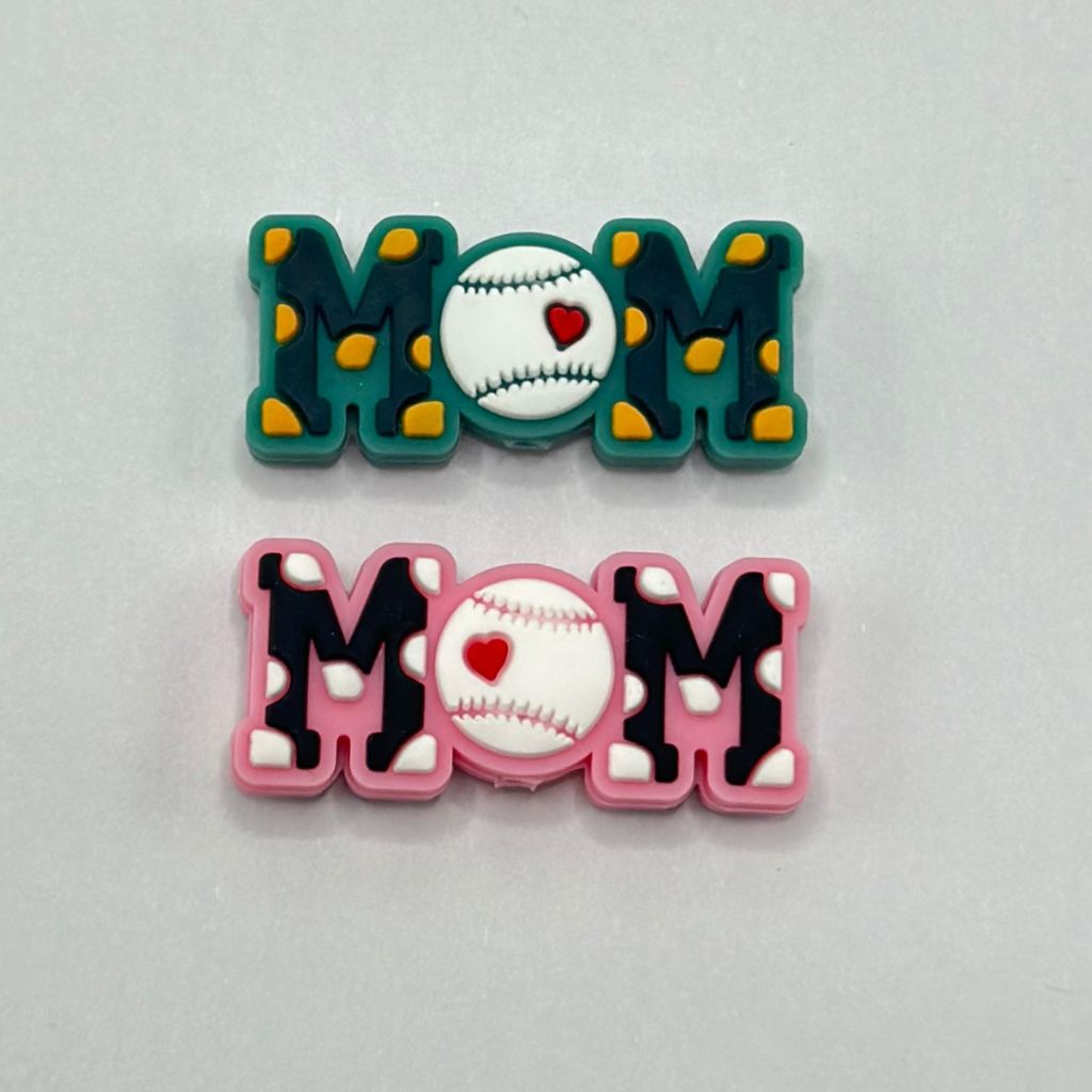 A set of two silicone beads with a baseball and heart design, one in green and the other in pink, both spelling out 'MOM'.


