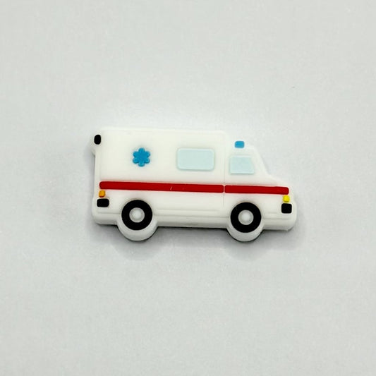 A white silicone bead in the shape of an ambulance with red and blue accents and a medical cross design on the side.


