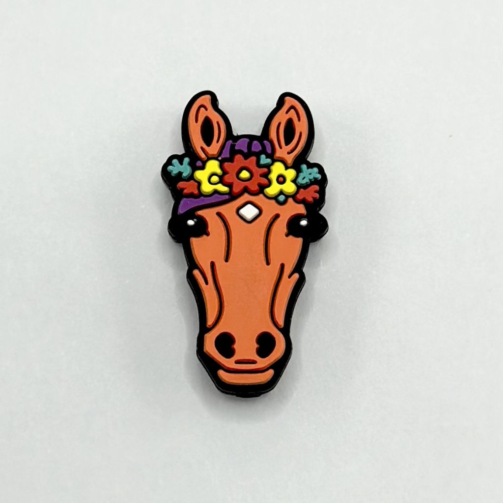 A silicone bead in the shape of a brown horse with a colorful flower garland on its head.

