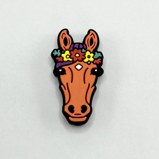 A silicone bead in the shape of a brown horse with a colorful flower garland on its head.

