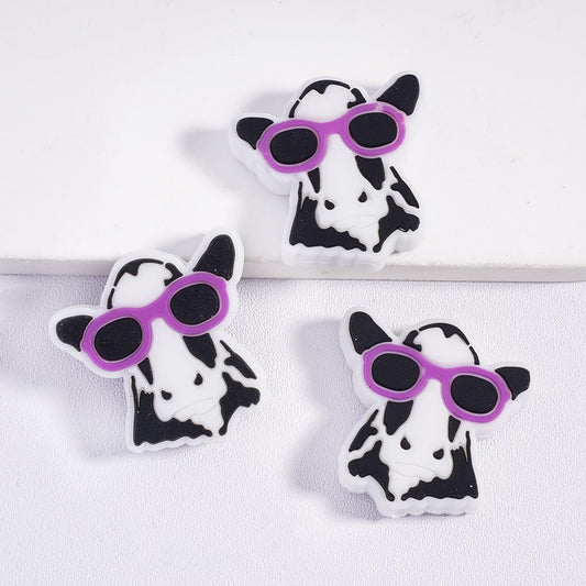 Three cow-shaped coasters with purple sunglasses on a white background