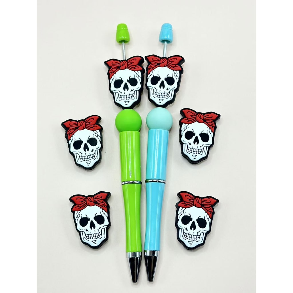 A collection of silicone beads shaped like skull skeleton heads with red bowknots on them, displayed on and off pens.