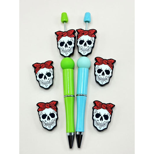 A collection of silicone beads shaped like skull skeleton heads with red bowknots on them, displayed on and off pens.